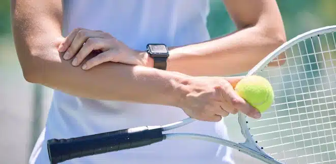 A woman playing tennis holds her elbow. If you experience elbow pain after sports, contact your doctor to find a way to treat tennis elbow.